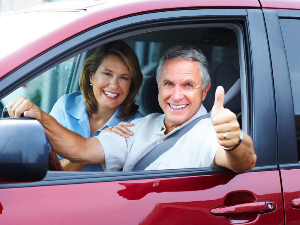 Smiling man and woman in a car, giving a thumbs up